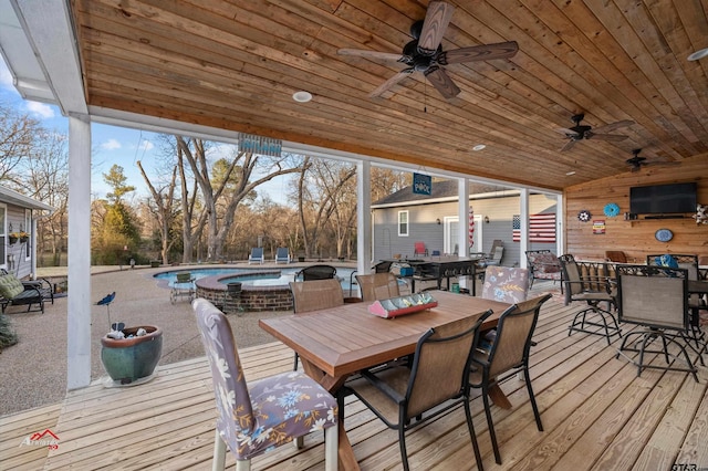 wooden terrace featuring outdoor dining space, a pool with connected hot tub, and a ceiling fan