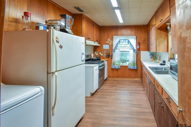 kitchen with wood walls, sink, appliances with stainless steel finishes, washer / dryer, and light wood-type flooring