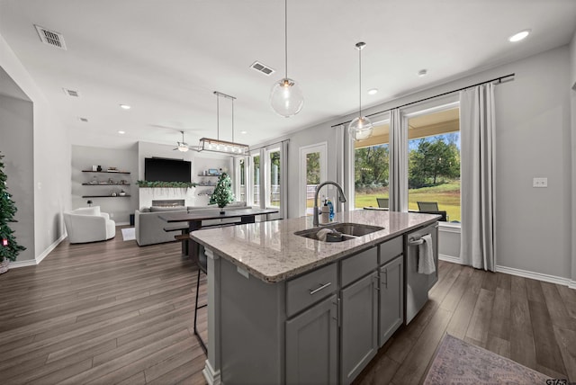 kitchen with a center island with sink, sink, dark hardwood / wood-style floors, ceiling fan, and light stone countertops