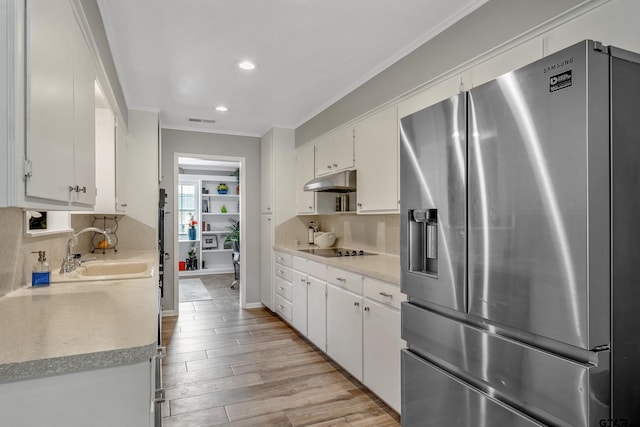 7411 Hollyoak Dr, Tyler, TX 75703 - kitchen with stainless steel fridge, crown molding, under cabinet range hood, white cabinets, and tasteful backsplash