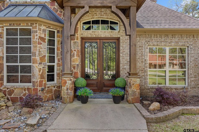 5875 Stonegate Trl, Tyler, TX 75703 - view of exterior entry with a shingled roof, french doors, brick siding, and stone siding