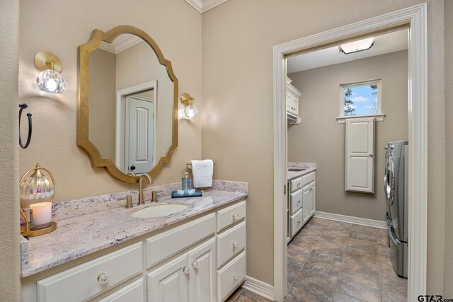 5875 Stonegate Trl, Tyler, TX 75703 - bathroom with washing machine and clothes dryer, vanity, baseboards, stone finish floors, and ornamental molding