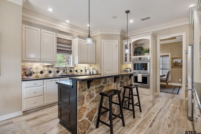 5875 Stonegate Trl, Tyler, TX 75703 - kitchen with double oven, dark countertops, a kitchen breakfast bar, light wood-type flooring, and ornamental molding