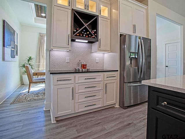 kitchen with stainless steel fridge with ice dispenser, white cabinetry, light wood-type flooring, and tasteful backsplash