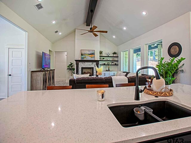 kitchen with light stone countertops, sink, a premium fireplace, beamed ceiling, and ceiling fan