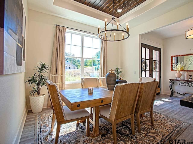 dining area with wood-type flooring, a raised ceiling, and ornamental molding