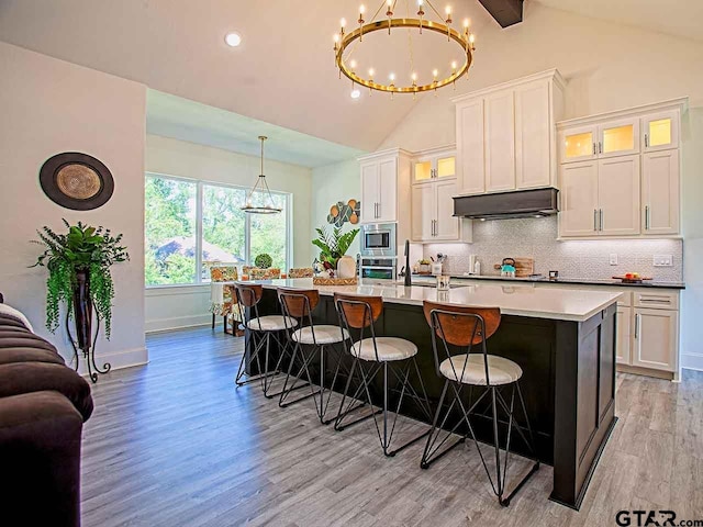 kitchen with white cabinets, stainless steel appliances, vaulted ceiling with beams, and light hardwood / wood-style flooring