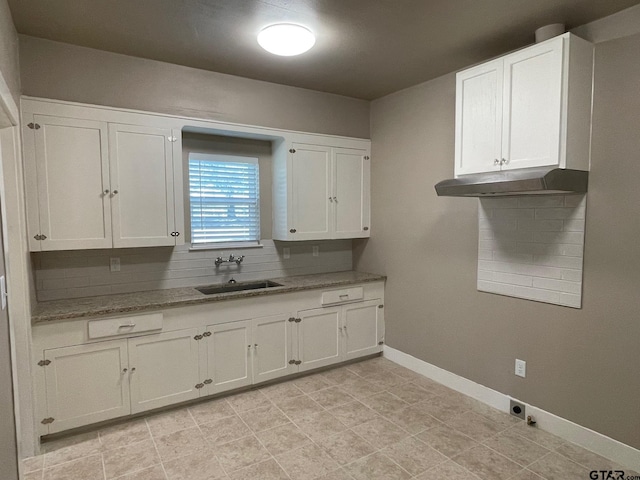 kitchen with white cabinets, backsplash, light stone countertops, and sink