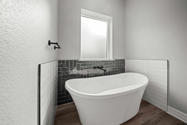 bathroom featuring hardwood / wood-style floors, a washtub, and tile walls