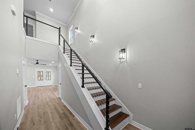 stairway featuring a wealth of natural light, crown molding, a towering ceiling, and wood-type flooring