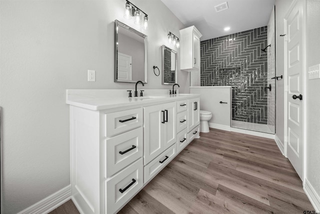 bathroom with a tile shower, vanity, hardwood / wood-style flooring, and toilet