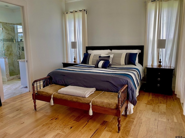 bedroom featuring light wood-type flooring, multiple windows, and connected bathroom