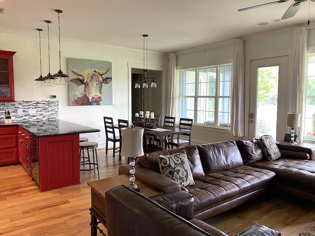 living room with light wood-type flooring, ornamental molding, and ceiling fan with notable chandelier