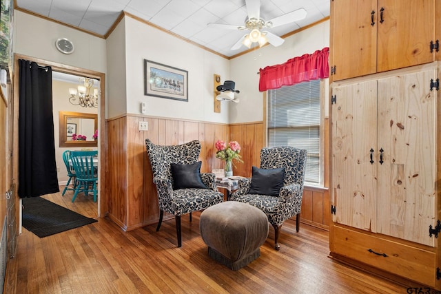 sitting room with ceiling fan with notable chandelier, wood-type flooring, and ornamental molding