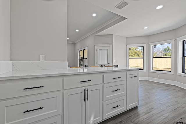 kitchen with crown molding, hardwood / wood-style floors, light stone counters, and white cabinets