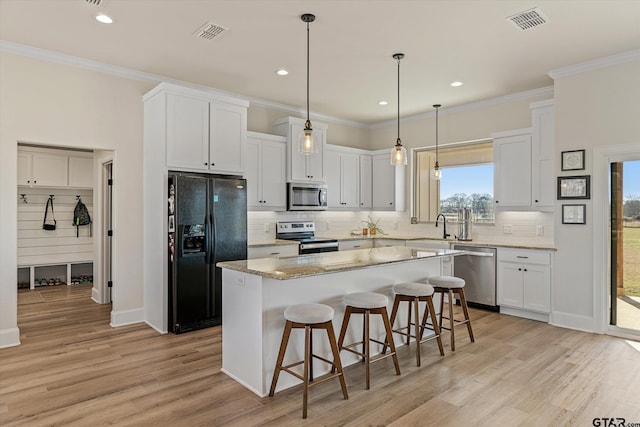 kitchen with appliances with stainless steel finishes, pendant lighting, light hardwood / wood-style flooring, white cabinets, and a kitchen island