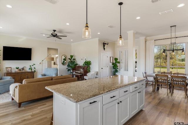 kitchen featuring pendant lighting, ceiling fan, light stone countertops, a kitchen island, and white cabinetry