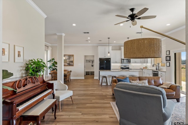 living room featuring ceiling fan, sink, crown molding, and light hardwood / wood-style flooring