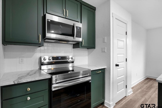 kitchen with light stone counters, stainless steel appliances, green cabinets, and backsplash