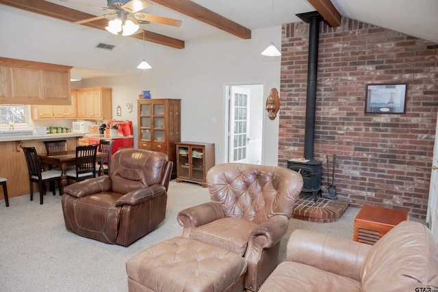 living room with brick wall, ceiling fan, carpet, a wood stove, and lofted ceiling with beams