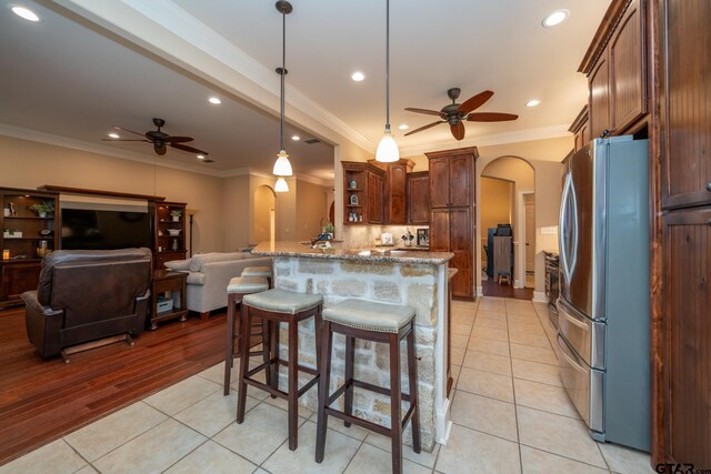 kitchen with stainless steel refrigerator, a breakfast bar, light stone countertops, light hardwood / wood-style flooring, and pendant lighting