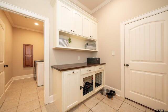 clothes washing area featuring cabinets, light tile patterned floors, washer and clothes dryer, and ornamental molding