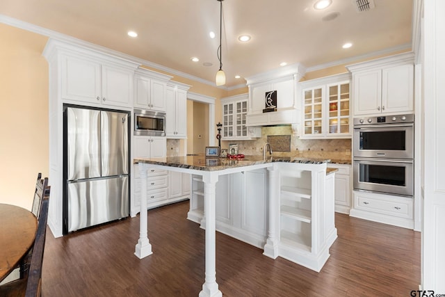 kitchen featuring white cabinets, decorative backsplash, dark stone countertops, appliances with stainless steel finishes, and a kitchen bar