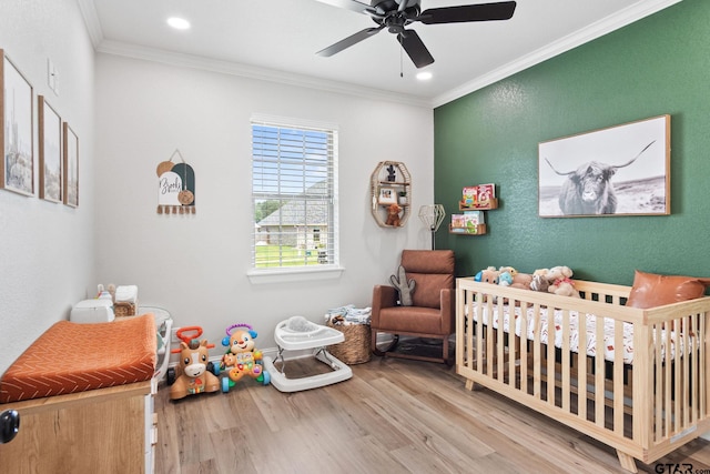 bedroom with hardwood / wood-style flooring, ceiling fan, a nursery area, and ornamental molding