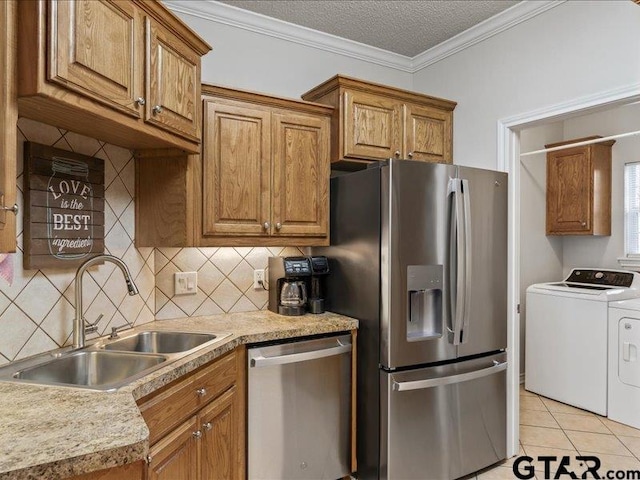 kitchen featuring sink, light tile patterned floors, appliances with stainless steel finishes, ornamental molding, and washing machine and clothes dryer