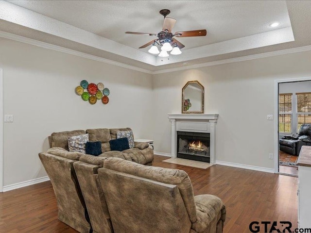 living room featuring ceiling fan, a tray ceiling, ornamental molding, a textured ceiling, and dark hardwood / wood-style flooring