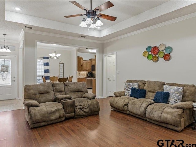 living room featuring crown molding, a tray ceiling, ceiling fan with notable chandelier, and hardwood / wood-style floors