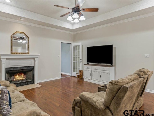 living room featuring hardwood / wood-style flooring, ornamental molding, ceiling fan, and a tray ceiling