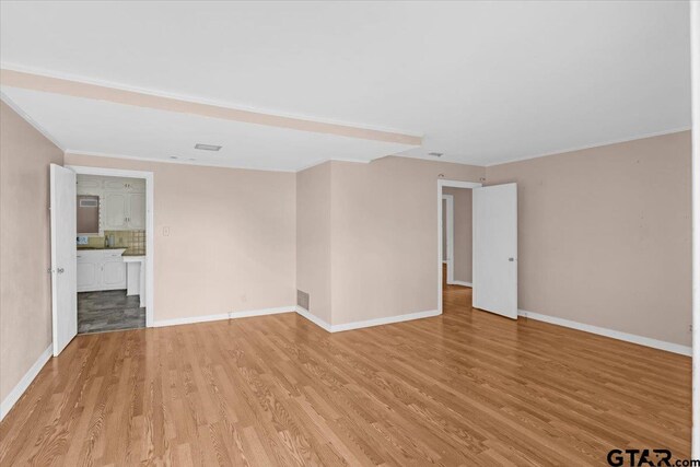 unfurnished room with crown molding, visible vents, light wood finished floors, and baseboards