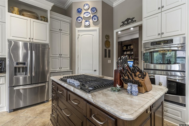 kitchen with white cabinetry, appliances with stainless steel finishes, ornamental molding, and light tile patterned floors