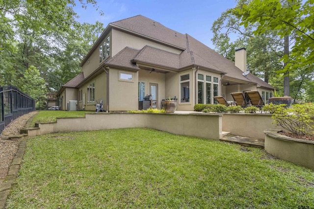 rear view of house featuring ceiling fan, a chimney, a lawn, central AC, and stucco siding