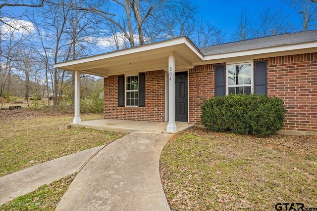 view of exterior entry with a lawn and a porch