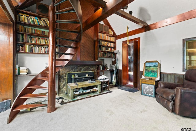 living room with a fireplace, wooden walls, vaulted ceiling with beams, and carpet floors