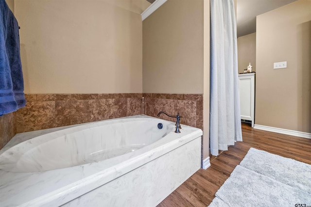 bathroom with a garden tub, wood finished floors, and baseboards