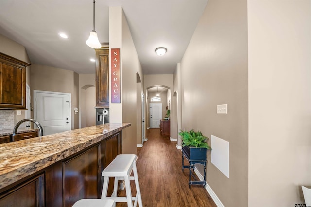 kitchen with baseboards, arched walkways, decorative backsplash, dark wood-type flooring, and a kitchen breakfast bar