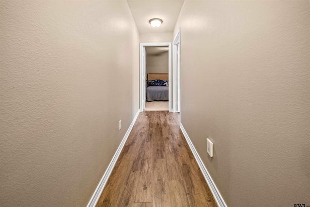 corridor with a textured wall, baseboards, and wood finished floors