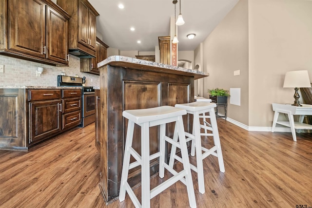 kitchen featuring tasteful backsplash, dark brown cabinetry, decorative light fixtures, light wood-type flooring, and stainless steel gas stove