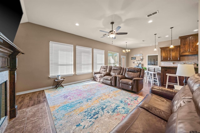 living area with ceiling fan with notable chandelier, dark wood finished floors, recessed lighting, a fireplace, and baseboards