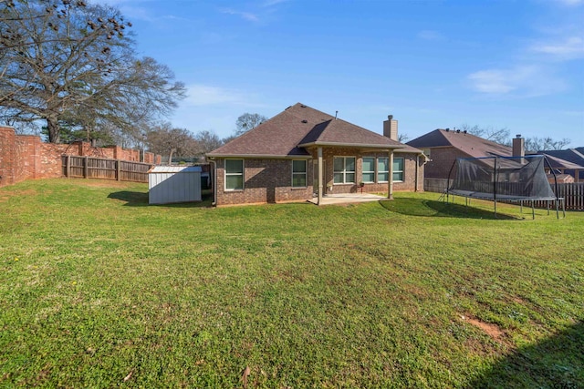 back of house with a shed, a fenced backyard, an outdoor structure, a trampoline, and brick siding