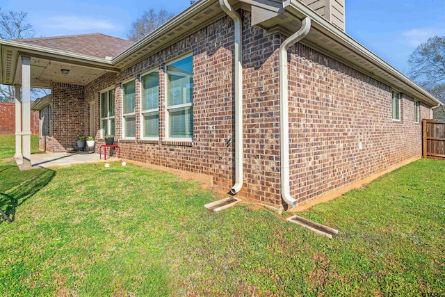 view of home's exterior featuring brick siding, a patio area, a lawn, and fence