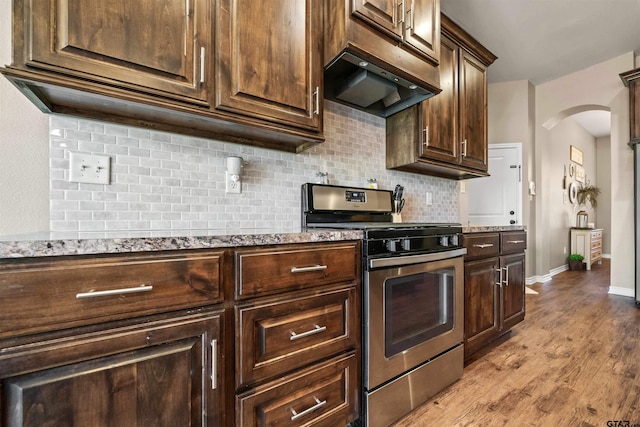 kitchen featuring backsplash, light wood-style flooring, arched walkways, custom exhaust hood, and stainless steel gas range