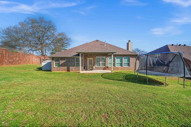 back of property featuring roof with shingles, a chimney, a trampoline, a lawn, and brick siding