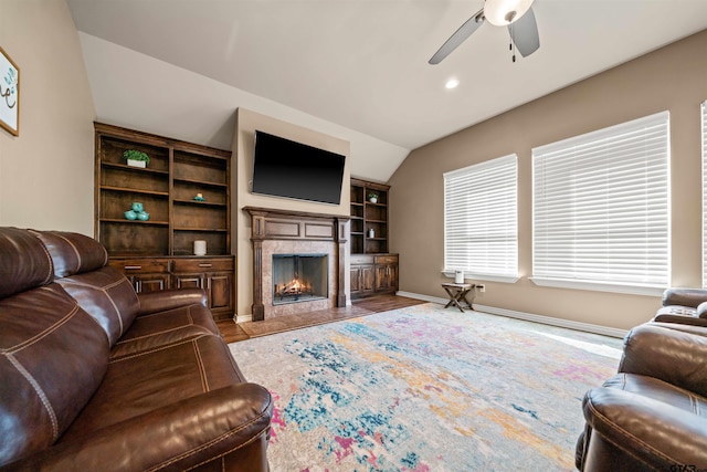 living area featuring baseboards, a fireplace with flush hearth, vaulted ceiling, wood finished floors, and a ceiling fan