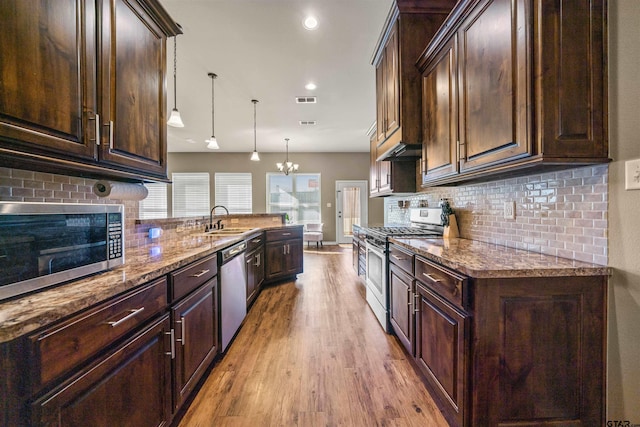 kitchen with a sink, light stone counters, stainless steel appliances, light wood finished floors, and dark brown cabinets