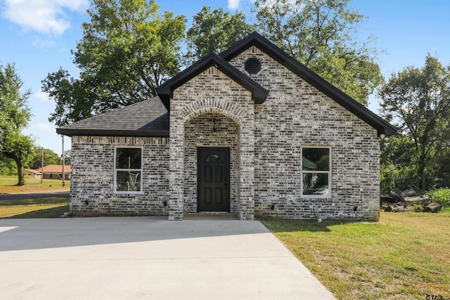 view of front of house featuring driveway, brick siding, roof with shingles, and a front yard