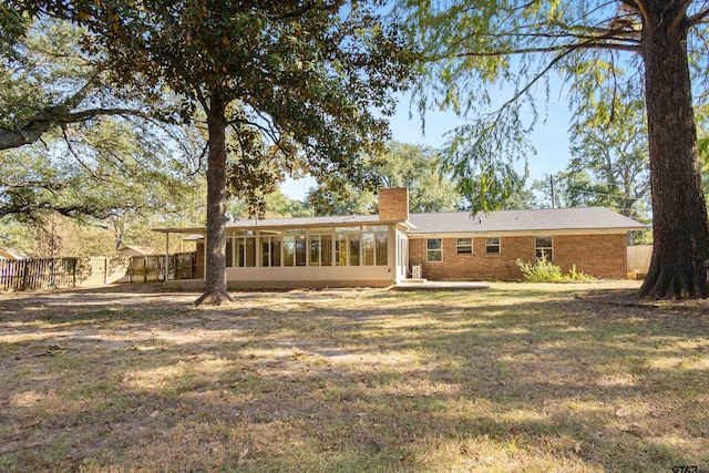 rear view of property featuring fence, a chimney, a sunroom, brick siding, and a lawn
